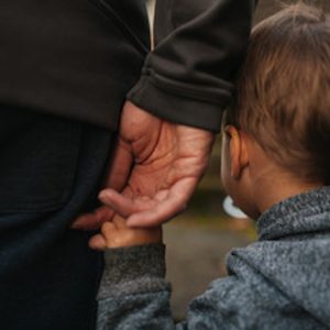 A child holds hands with a parent, showcasing a tender moment between them in a casual outdoor setting.