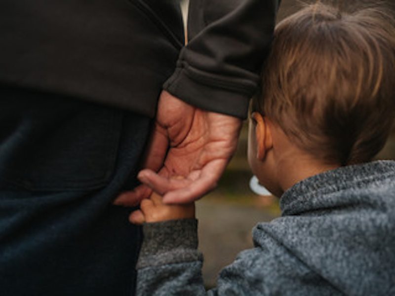 A child holds hands with a parent, showcasing a tender moment between them in a casual outdoor setting.
