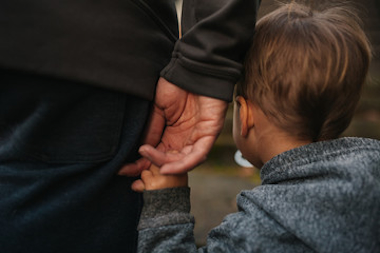 A child holds hands with a parent, showcasing a tender moment between them in a casual outdoor setting.