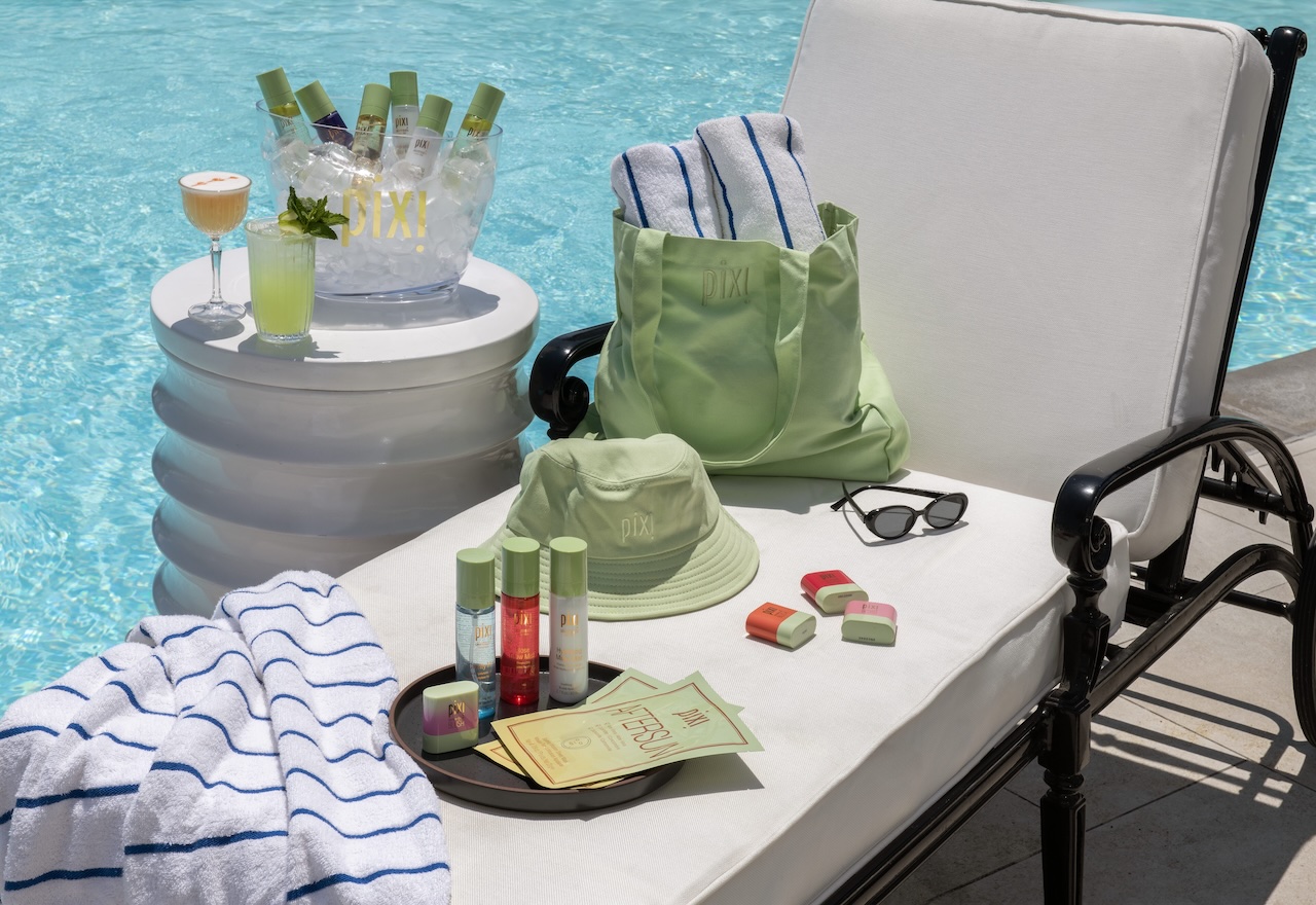 Summer glow-up essentials from Pixi Beauty by the pool, featuring products, drinks, and a green bag on a lounge chair.