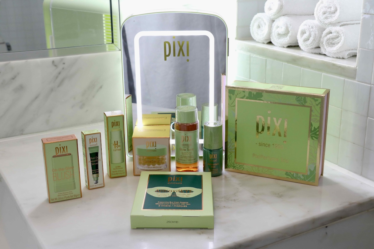 Pixi Beauty products arranged on a marble countertop, featuring skincare and makeup items alongside a mirror in a bathroom setting.