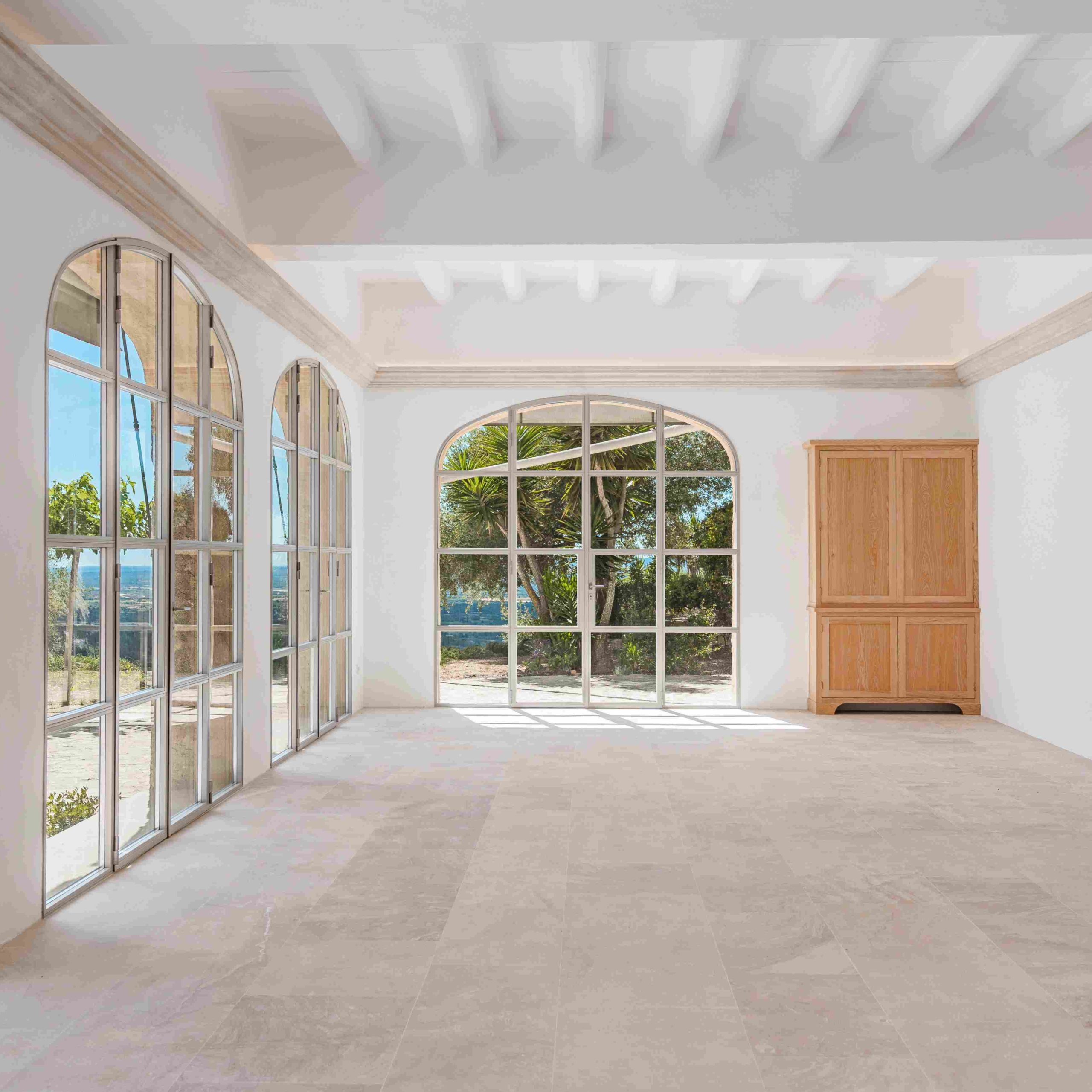 Bright and spacious interior of a Mallorca hilltop estate with arched windows showcasing Mediterranean views.