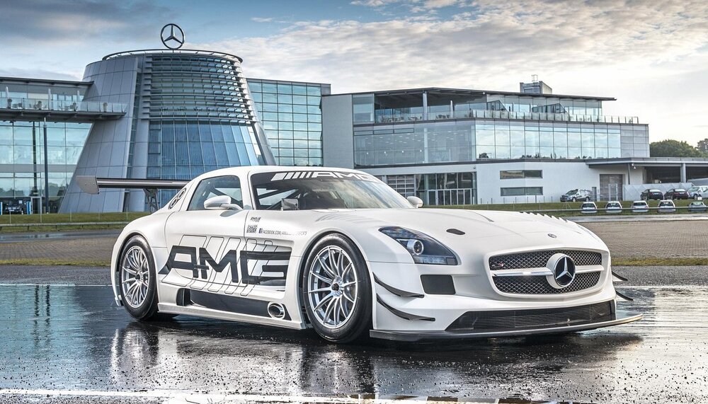 A Mercedes-Benz SLS AMG sports car parked in front of a modern building, reflecting on a wet surface.