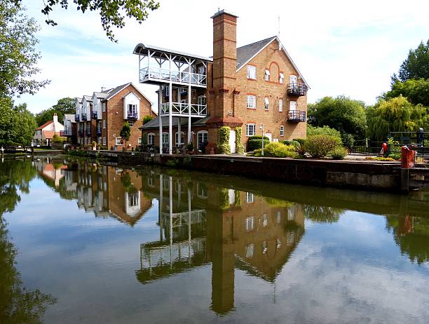 Reflective waterside view of charming buildings in Weybridge, surrounded by lush greenery.