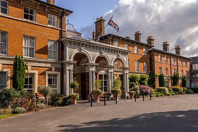 Oatlands Park Hotel's elegant entrance surrounded by lush plants and flowers, showcasing the charm of Surrey's countryside.
