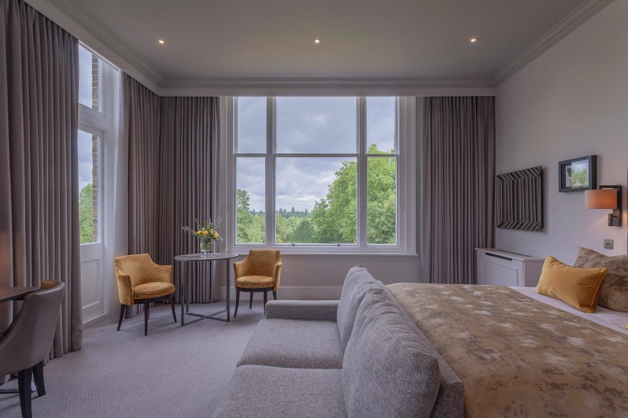 Spacious hotel room featuring large windows with views of greenery, modern furnishings, and a cozy seating area.