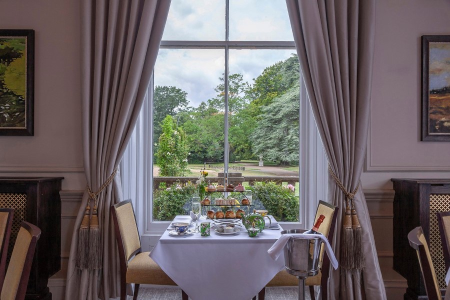 Afternoon tea set on a table by a window, showcasing a view of lush greenery and elegant decor in a hotel setting.
