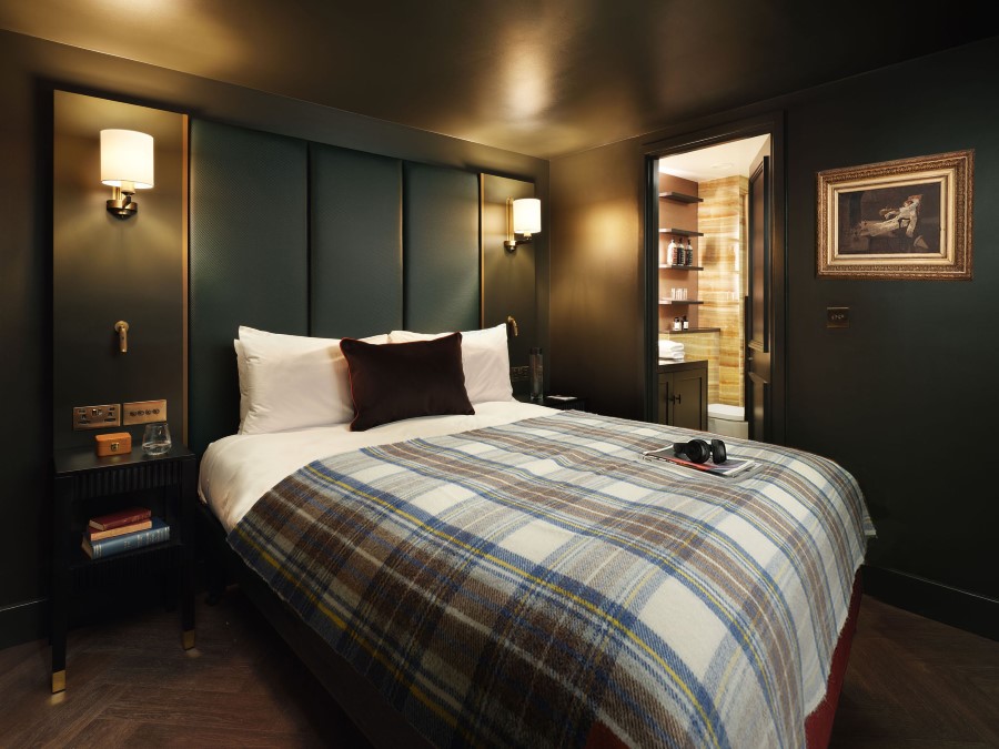 Cozy hotel room featuring a plush bed with a plaid throw, warm lighting, and an adjoining bathroom.