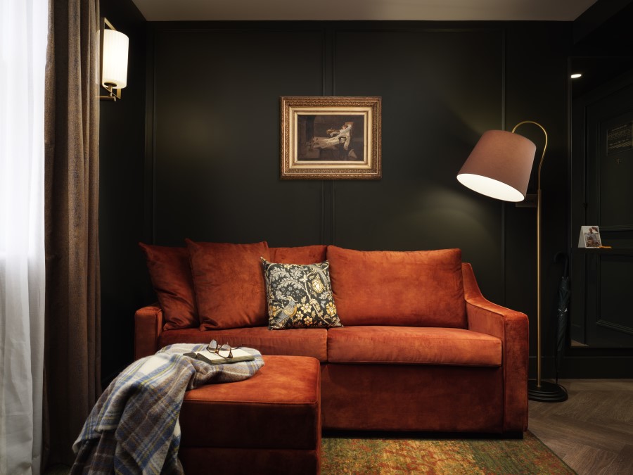 Cozy living room featuring an orange sofa with decorative pillows, a floor lamp, and framed artwork against a dark wall.