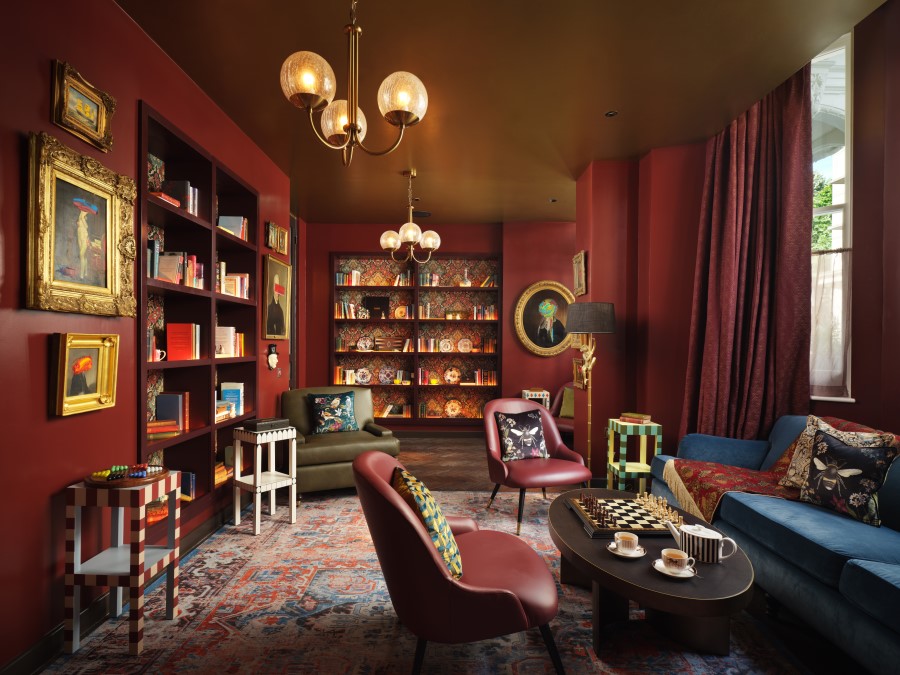 Cozy library with rich red walls, stylish furniture, and shelves filled with books, creating a sophisticated, inviting atmosphere.