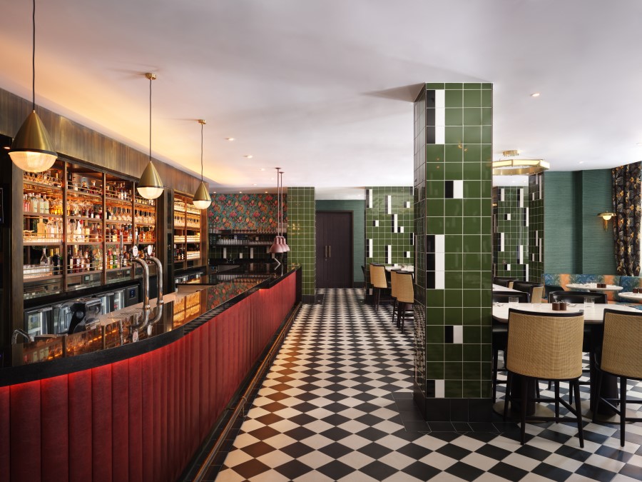 Elegant bar area featuring a vibrant green tile column, checkerboard floor, and warm lighting, creating a sophisticated atmosphere.