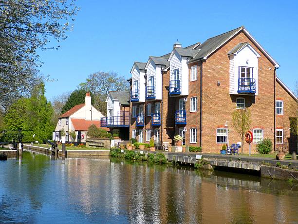 Canal-side residences in Weybridge with brick facades and blue balconies, under a clear blue sky.