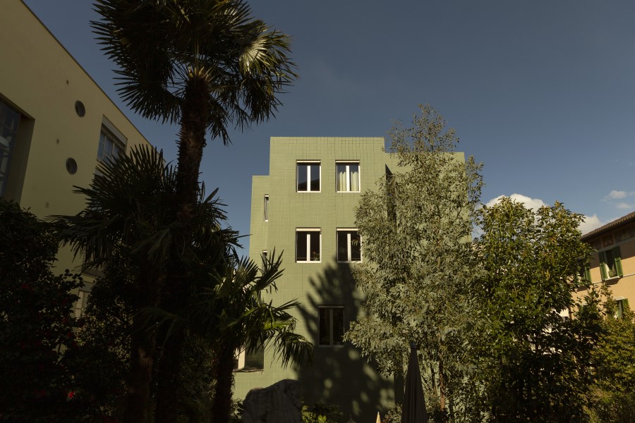 The green facade of B5 Boutique Hotel is framed by lush trees and palm plants against a clear sky.