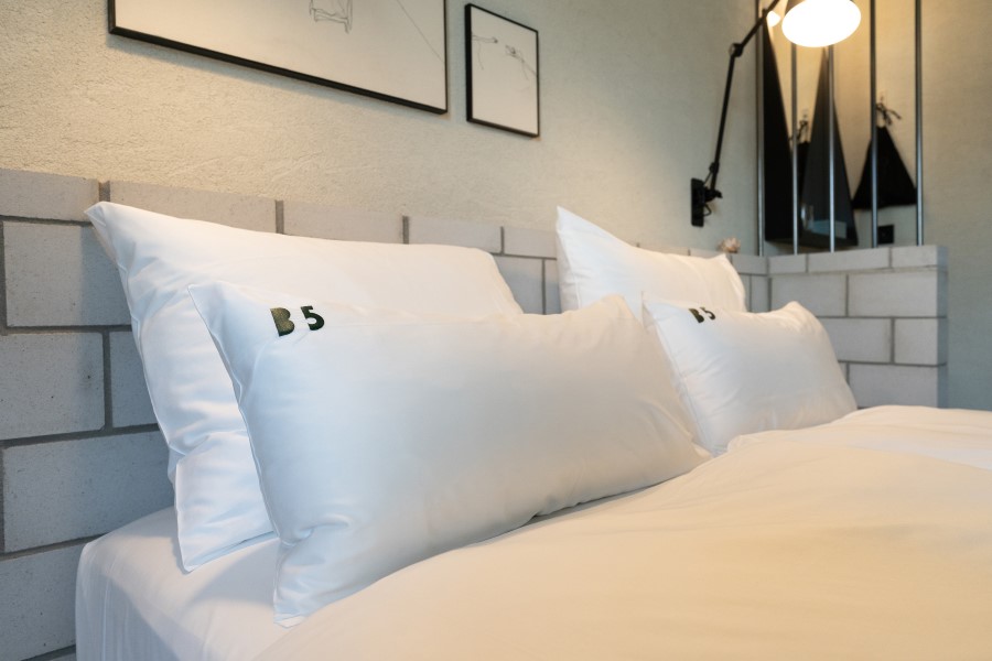 Stylish white bedding with embroidered "B5" pillows in a modern hotel room setting.