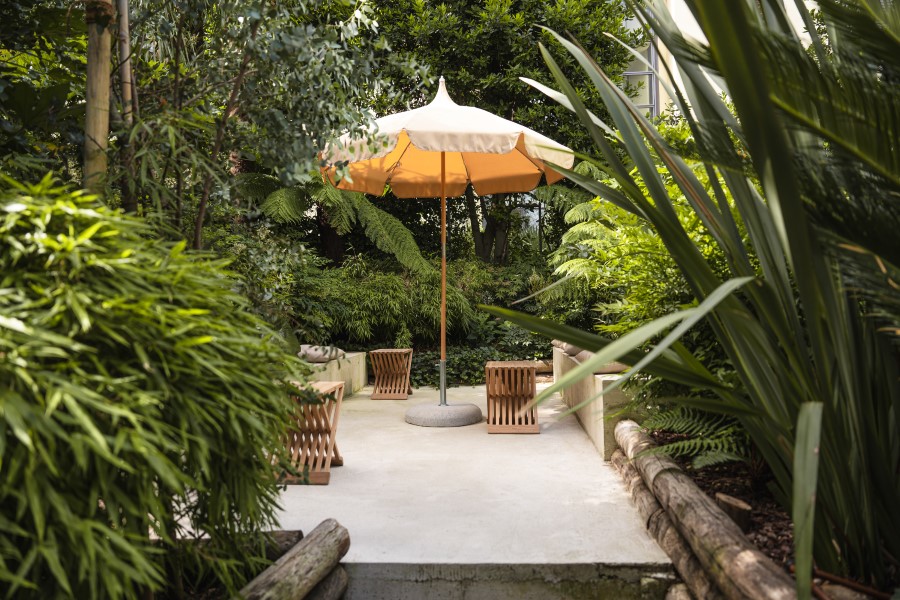 A serene garden area with a large orange umbrella and wooden seating surrounded by lush greenery at B5 Boutique Hotel Lugano.