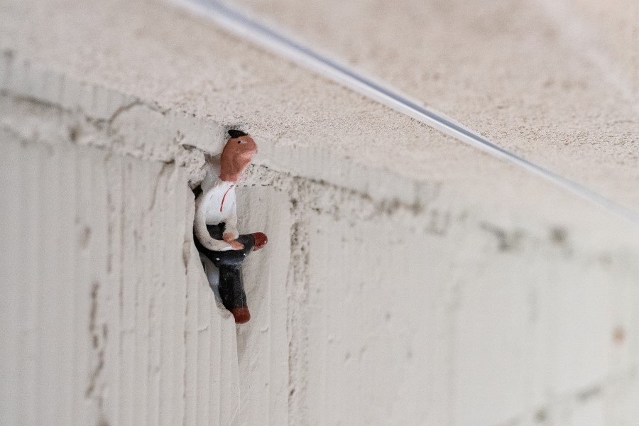 A small, figurine of a seated man on a textured white wall near the top edge.