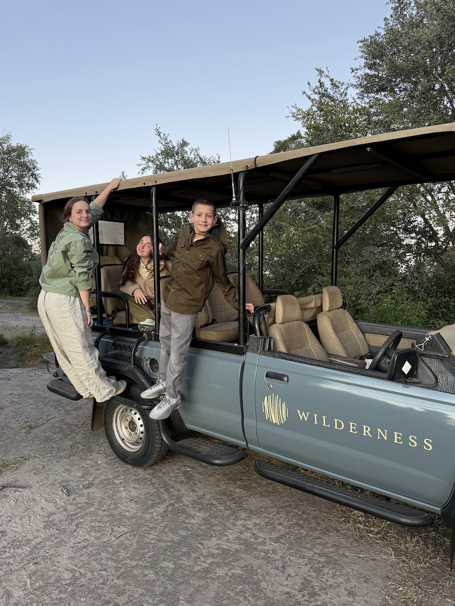 Three children playfully pose on a safari vehicle in a natural setting during their adventure in Zambia.