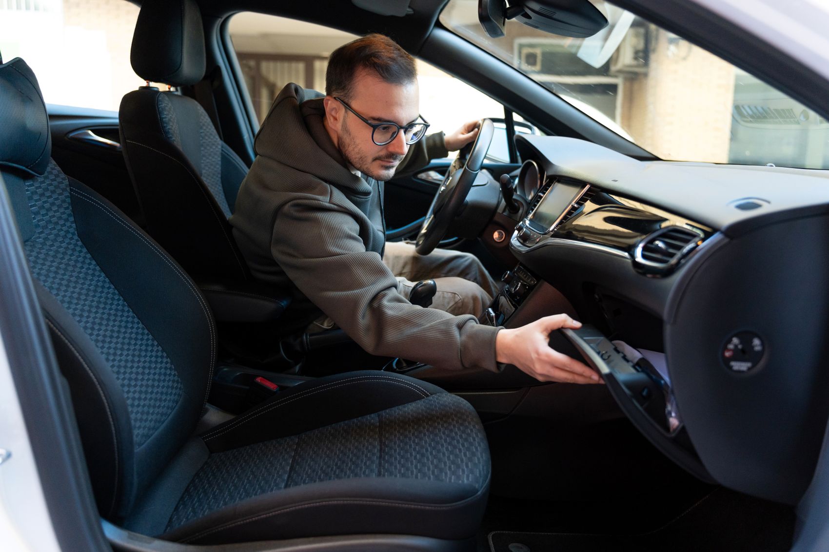 A person reaching for an item in the glove compartment of a car's interior.