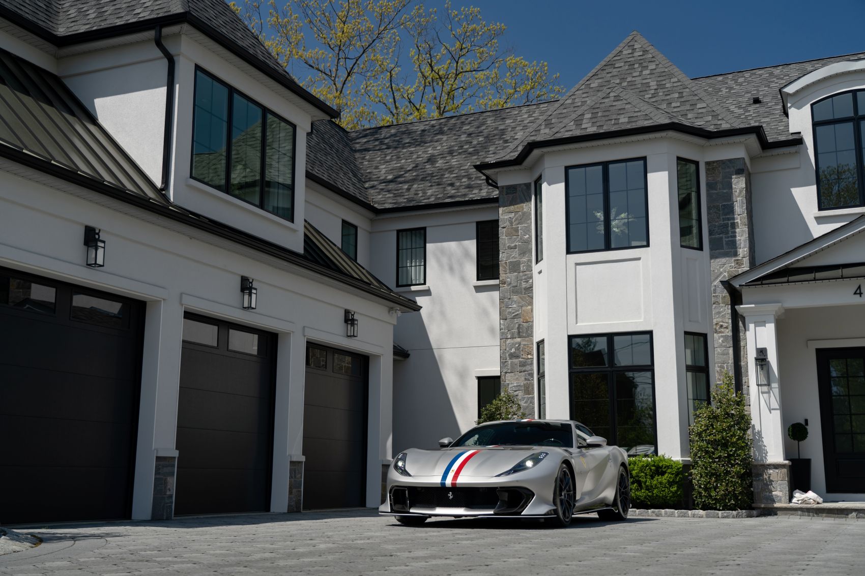 Luxury home with a silver sports car parked in the driveway, showcasing modern architecture and elegant landscaping.