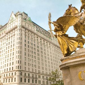 The historic Plaza Hotel features ornate architecture and a golden statue in the foreground against a clear sky.