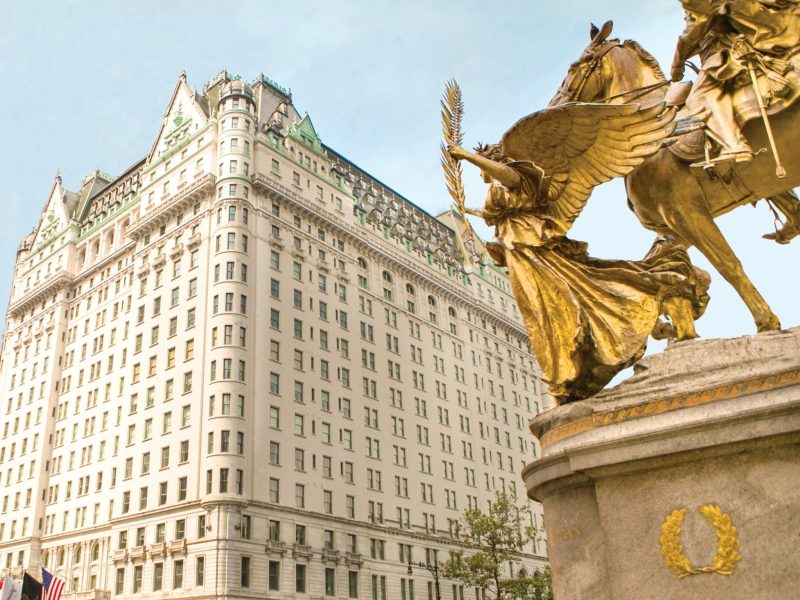 The historic Plaza Hotel features ornate architecture and a golden statue in the foreground against a clear sky.
