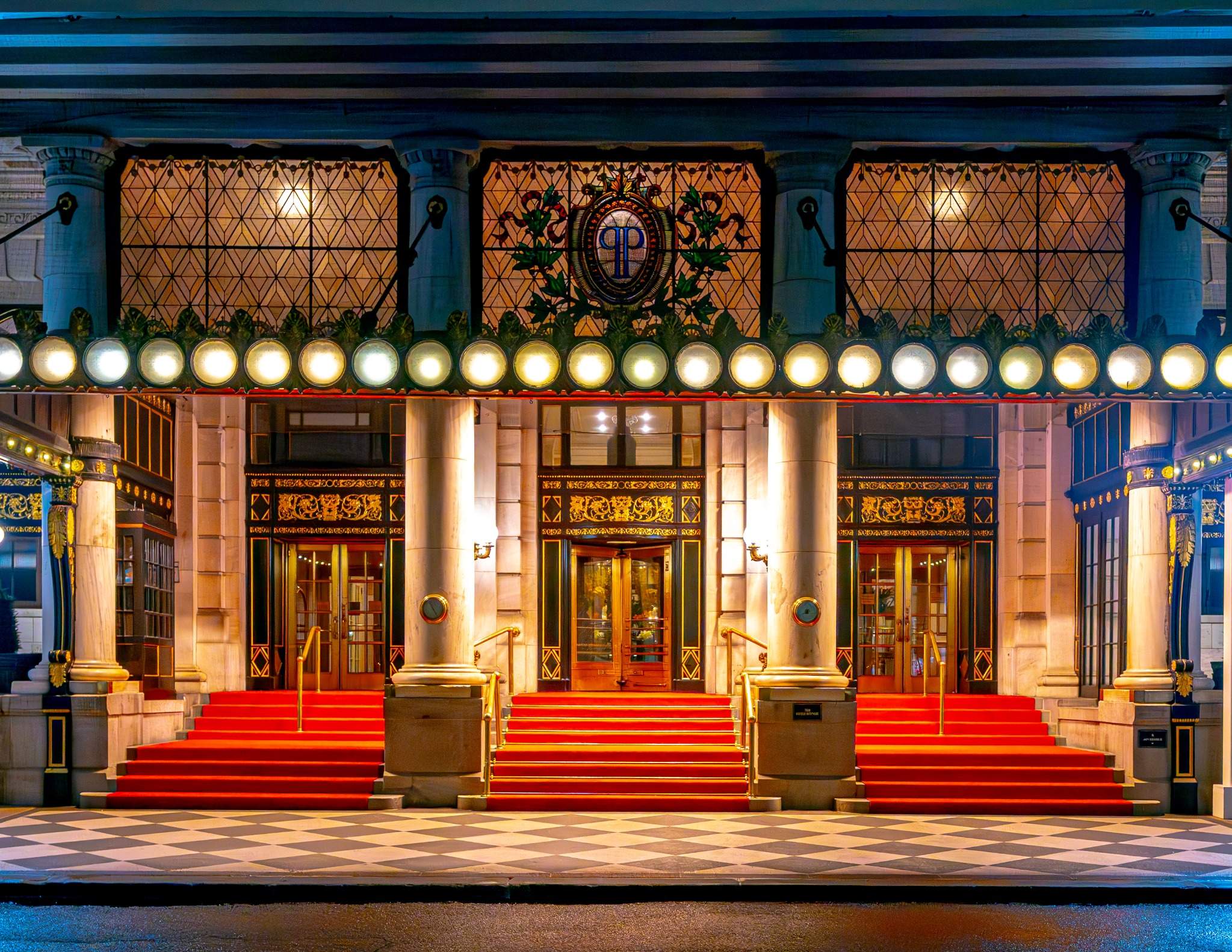 The grand entrance of The Plaza Hotel, featuring red carpeted steps and ornate architecture with glowing lights at night.