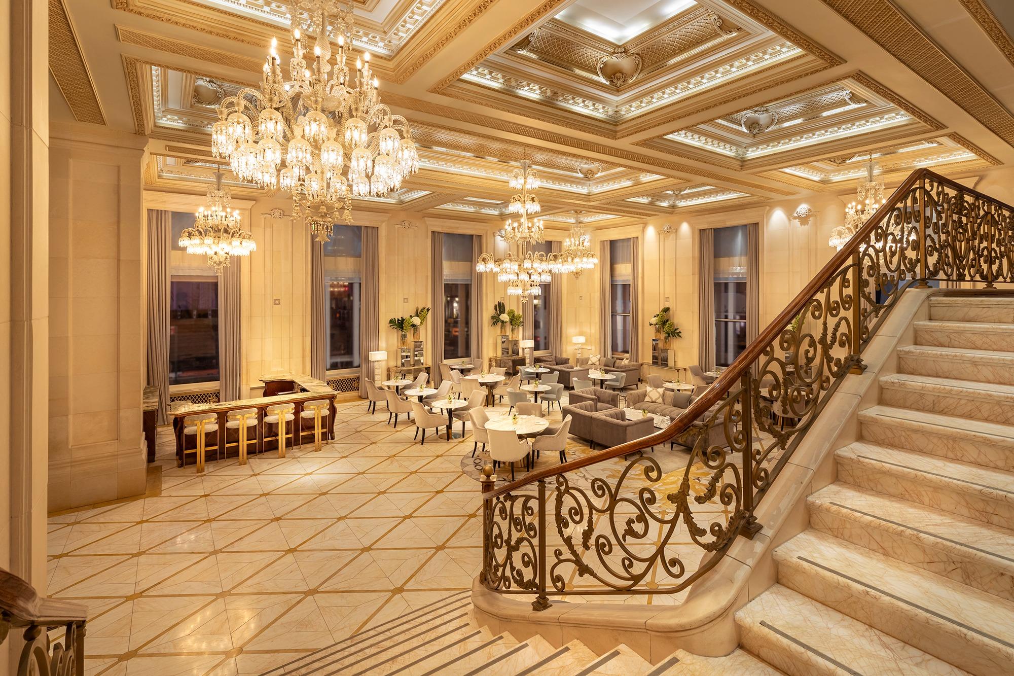 Elegant interior of the Champagne Bar at The Plaza New York, featuring chandeliers, plush seating, and a grand staircase.