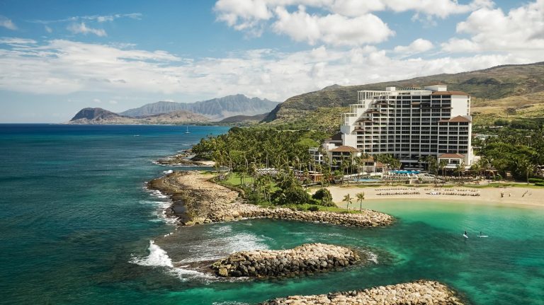 Four Seasons Oʻahu at Ko Olina features lush gardens and a stunning beachfront view surrounded by tropical mountains.