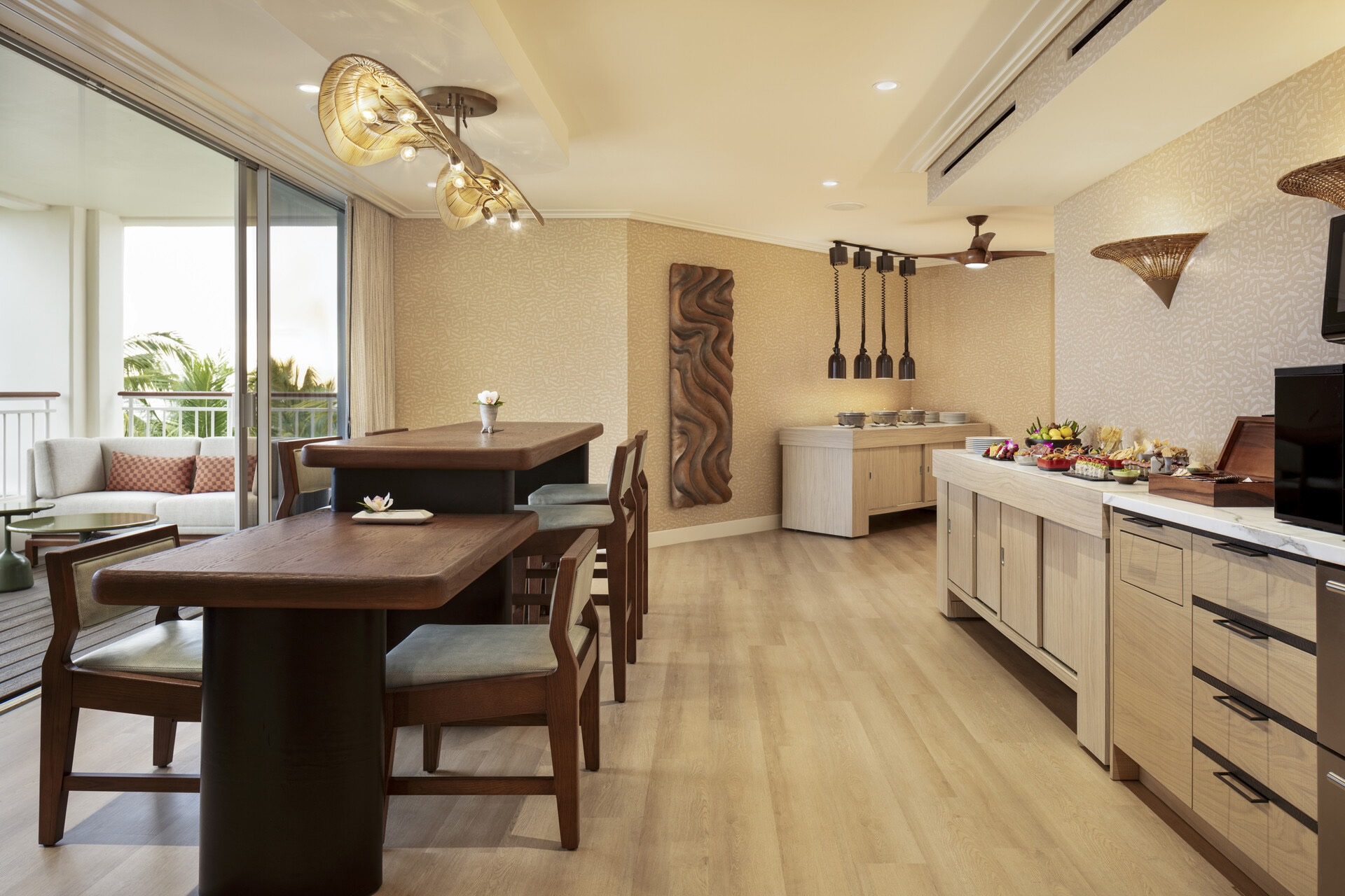 Elegant lounge area featuring a wooden table, stylish chairs, and a buffet with assorted dishes, overlooking lush greenery.