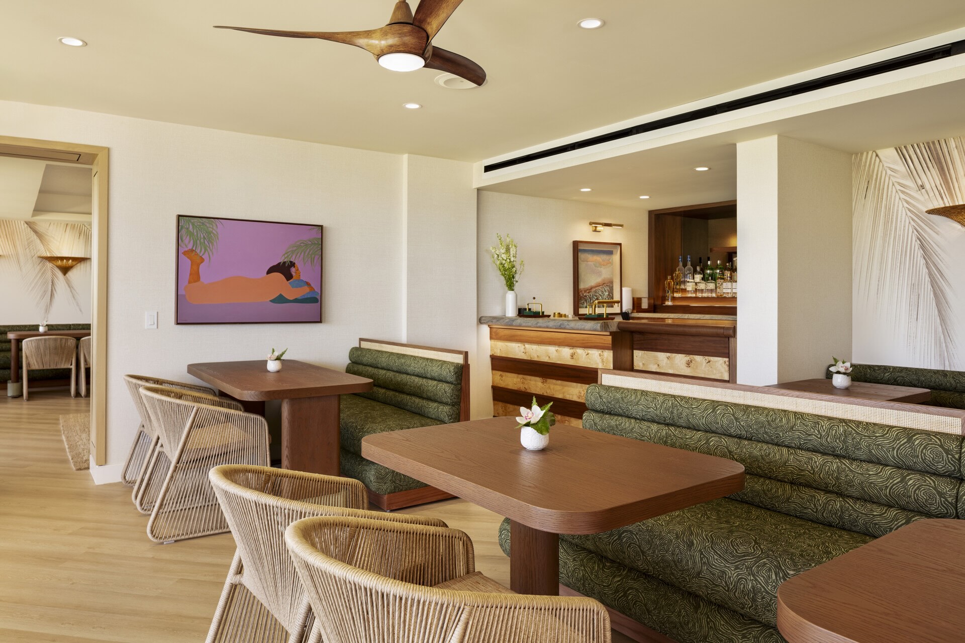 Stylish club lounge interior at Four Seasons Oʻahu, featuring cozy seating, a bar, and tropical artwork on the walls.
