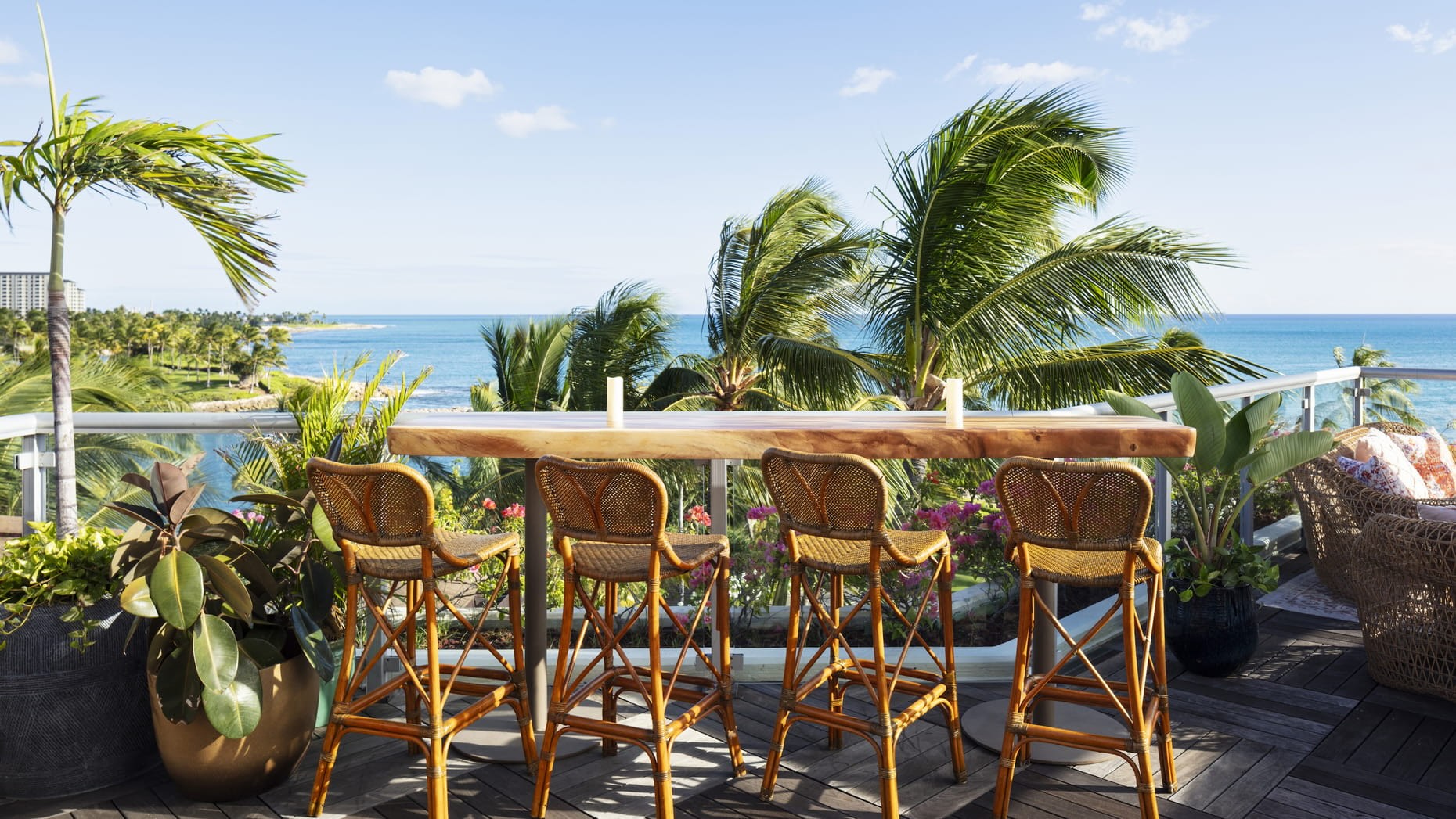 A beachfront bar with wooden stools and tropical plants, overlooking palm trees and the ocean at Four Seasons O’ahu.