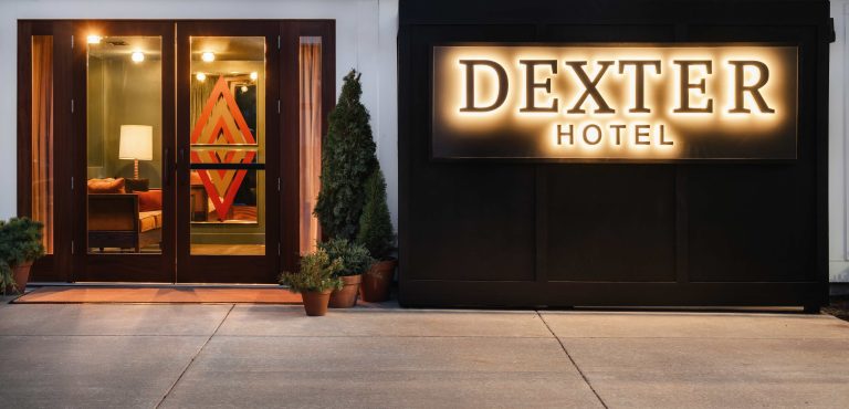 The entrance of Dexter Hotel features a stylish design with a illuminated sign and potted greenery along the walkway.