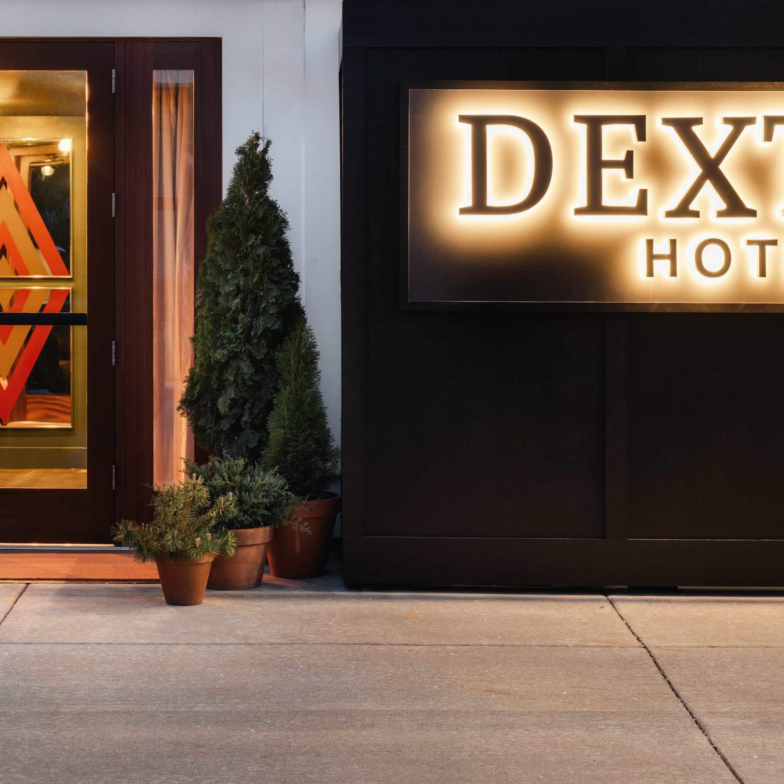 The entrance of Dexter Hotel features a stylish design with a illuminated sign and potted greenery along the walkway.