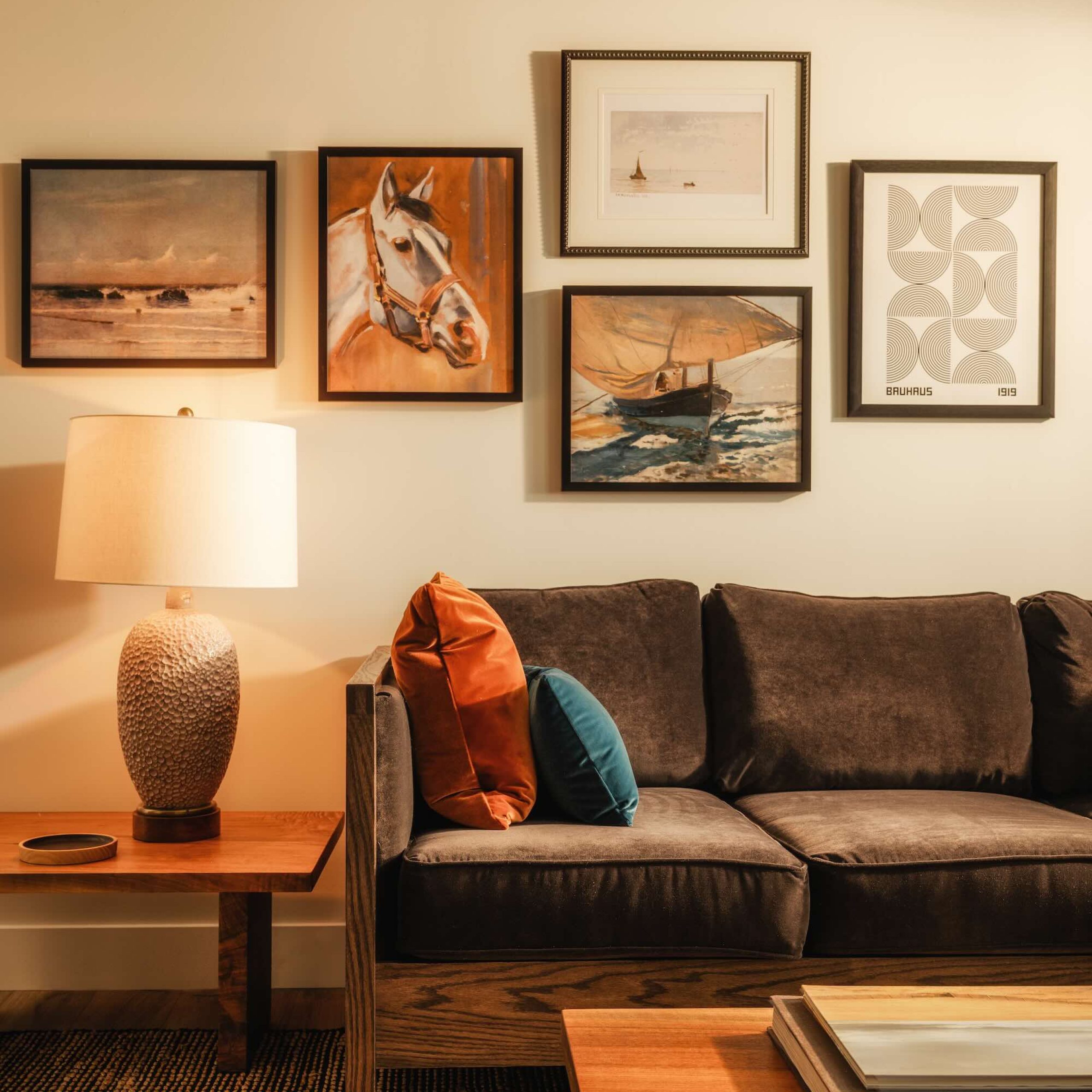 Cozy hotel living space with a plush sofa, decorative pillows, a lamp, and framed artwork on the wall.