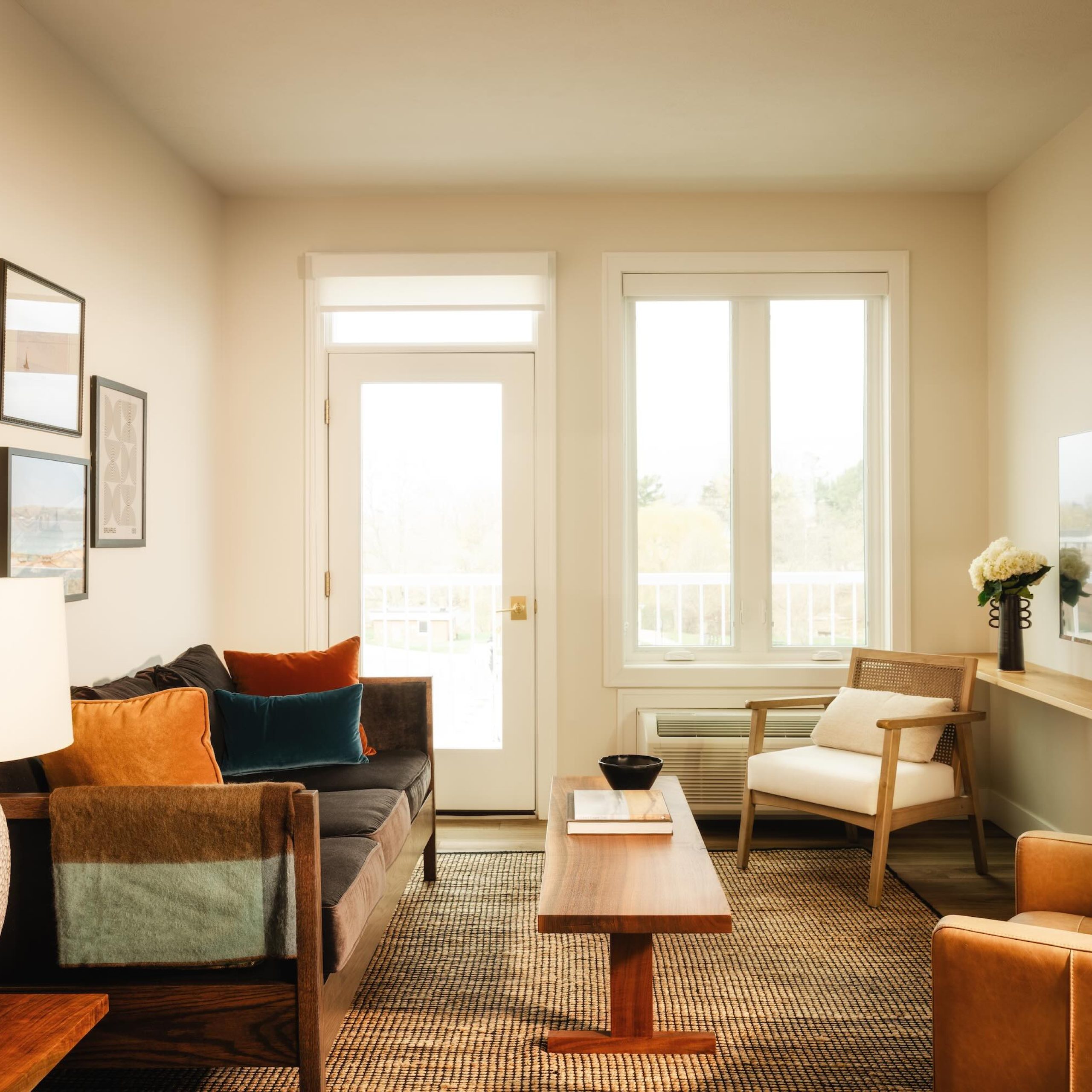 Cozy hotel living room featuring a sofa with colorful pillows, a wooden coffee table, and a TV mounted on the wall.