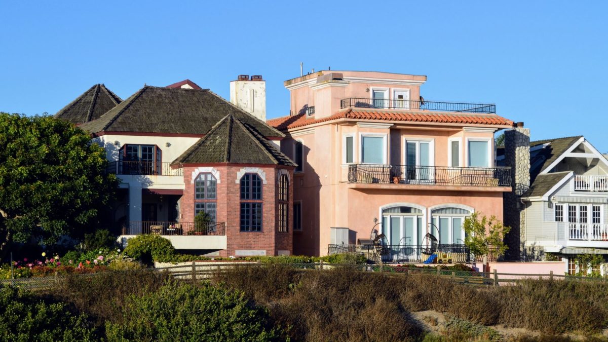 Stylish coastal homes featuring diverse architectural designs against a clear blue sky, embodying a boutique hotel aesthetic.