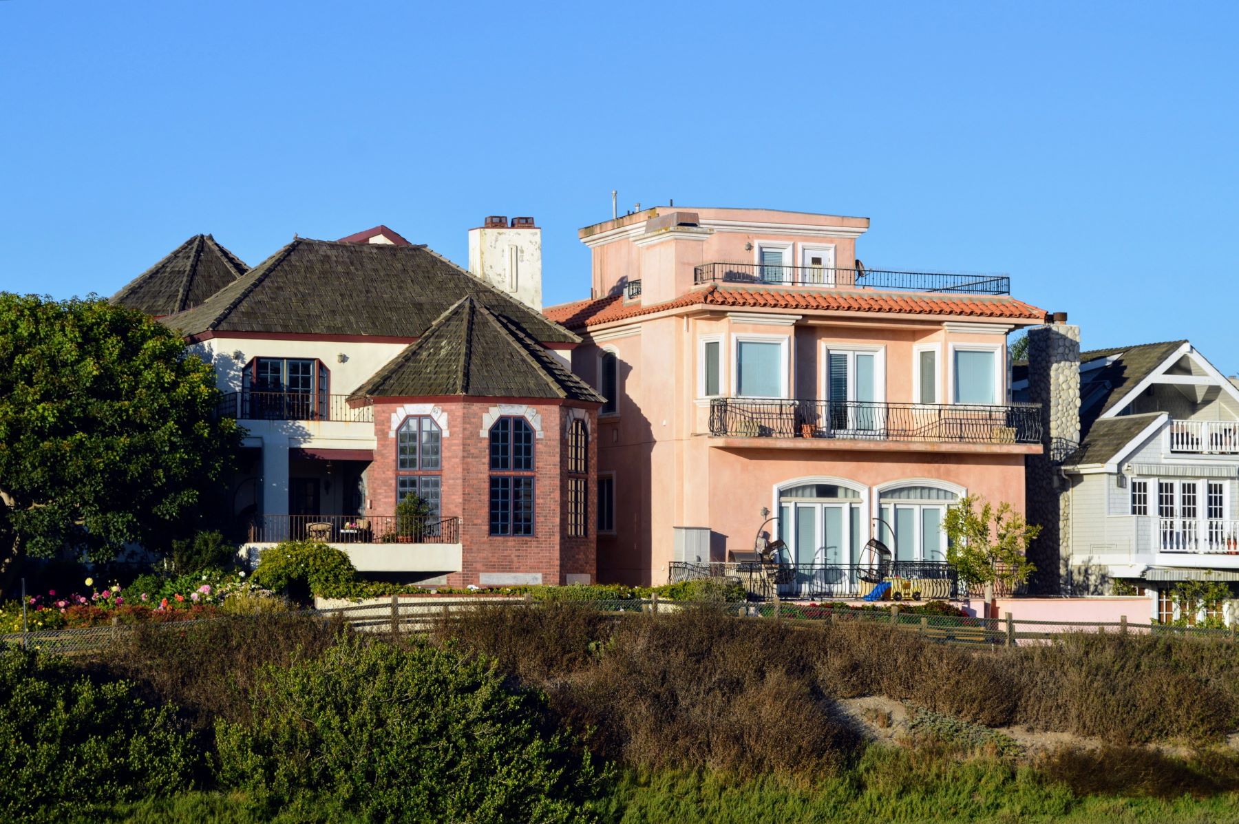 Stylish coastal homes featuring diverse architectural designs against a clear blue sky, embodying a boutique hotel aesthetic.