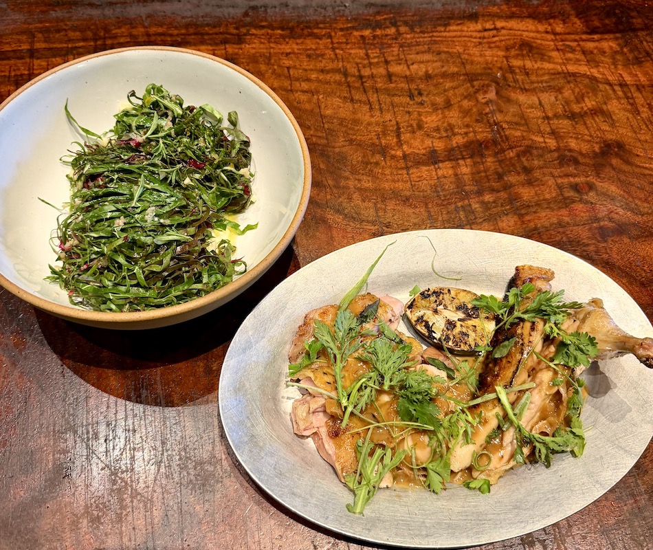 Grilled chicken garnished with herbs served alongside a bowl of fresh greens at The Charter Oak Restaurant.