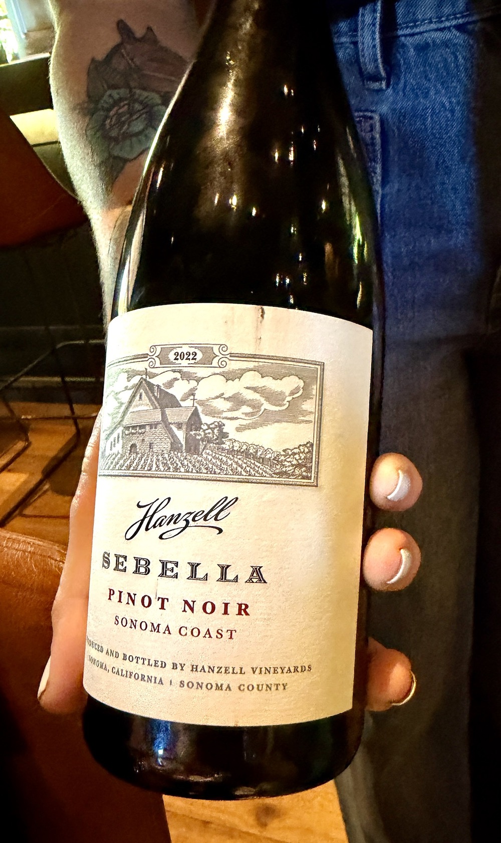 Hanzell Sebella Pinot Noir 2022 bottle held, showcasing its label with vineyard artwork, from Sonoma Coast, California.