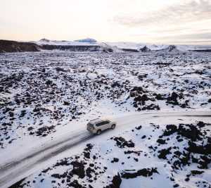 A vehicle drives along a snow-covered road in a volcanic landscape in Iceland.
