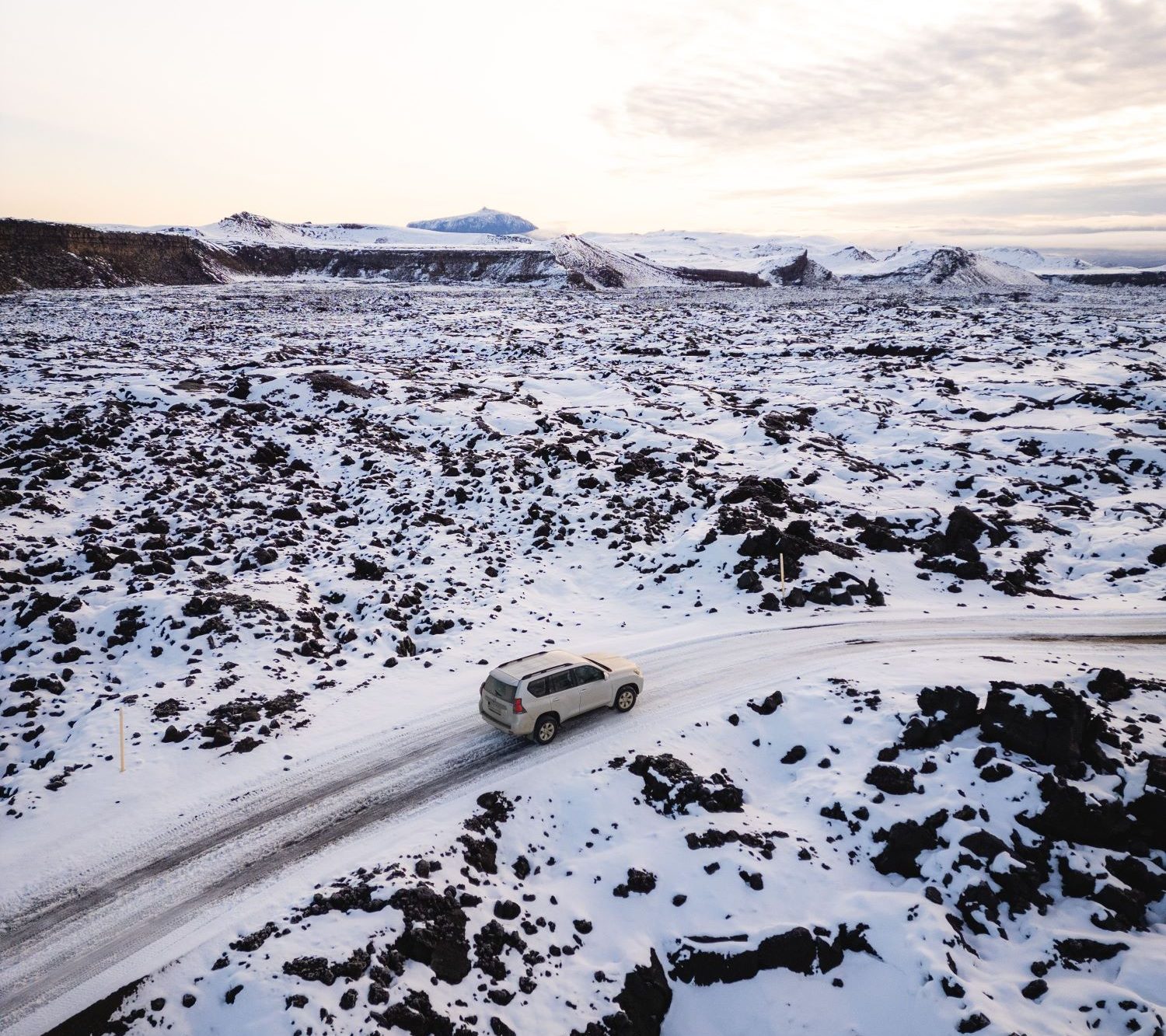 A vehicle drives along a snow-covered road in a volcanic landscape in Iceland.