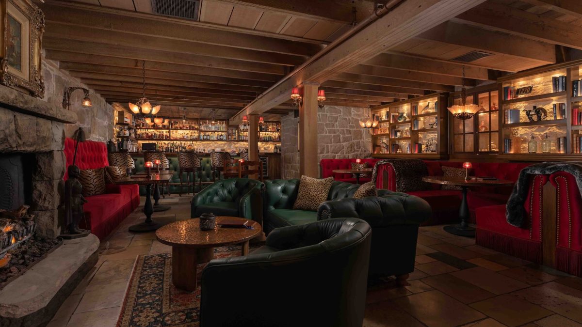 Luxurious interior of The Speakeasy at San Ysidro Ranch, featuring plush seating, a stone fireplace, and a well-stocked bar.