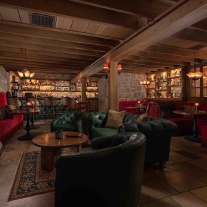Luxurious interior of The Speakeasy at San Ysidro Ranch, featuring plush seating, a stone fireplace, and a well-stocked bar.