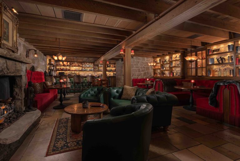 Luxurious interior of The Speakeasy at San Ysidro Ranch, featuring plush seating, a stone fireplace, and a well-stocked bar.