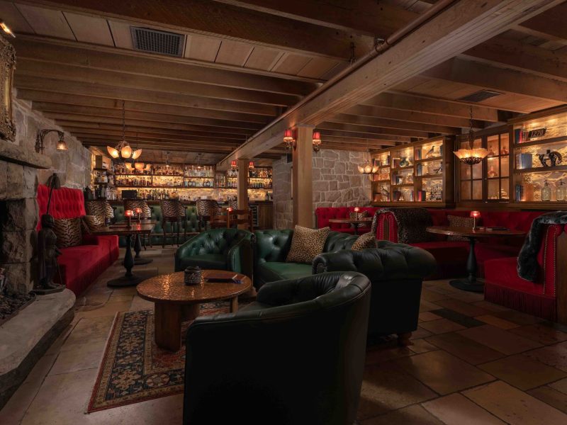 Luxurious interior of The Speakeasy at San Ysidro Ranch, featuring plush seating, a stone fireplace, and a well-stocked bar.
