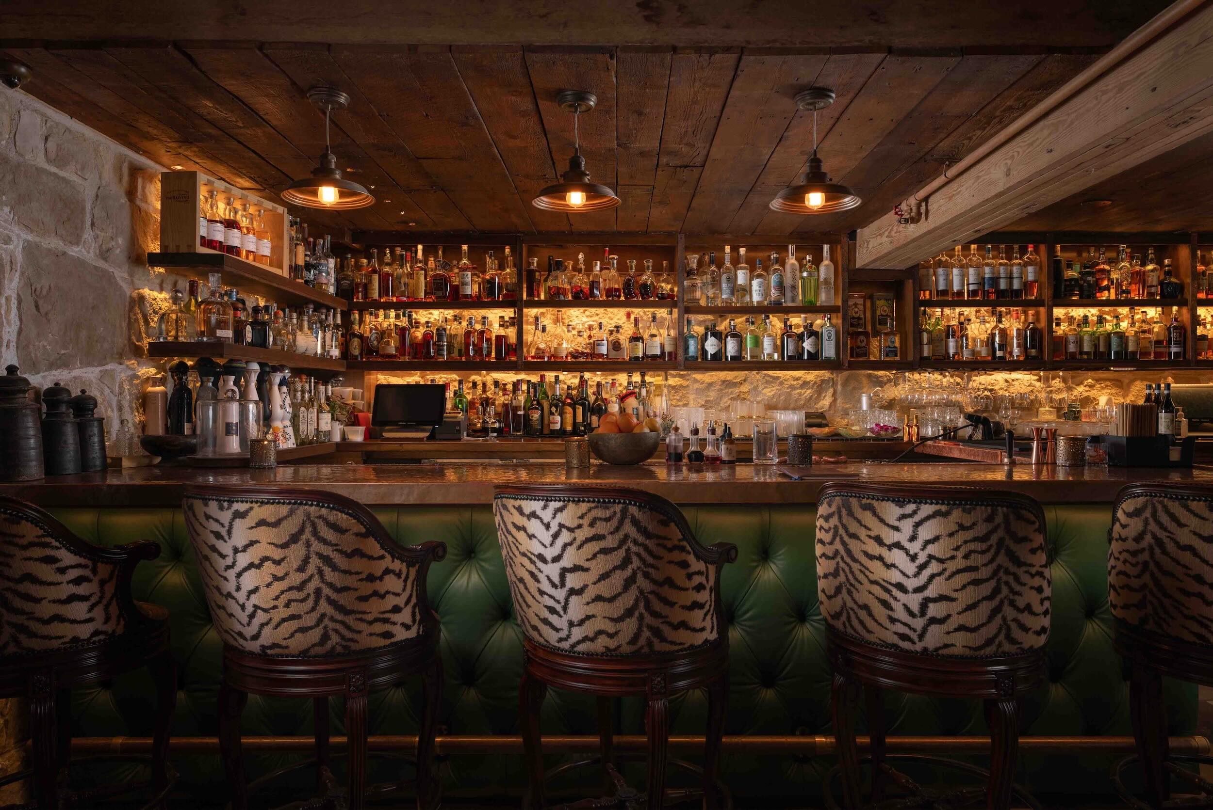 Elegant bar interior featuring a wide selection of spirits, rustic wood accents, and distinctive animal-print upholstered chairs.