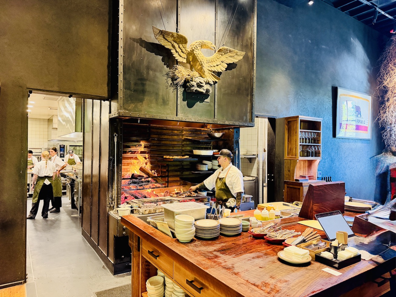 A bustling kitchen at The Charter Oak with chefs preparing food by a wood-fired grill and a rustic dining setup.