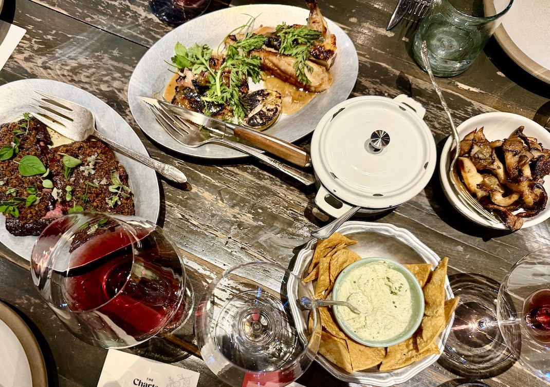 A beautifully arranged dining table featuring grilled meats, sides, dips, and glasses of red wine at The Charter Oak.