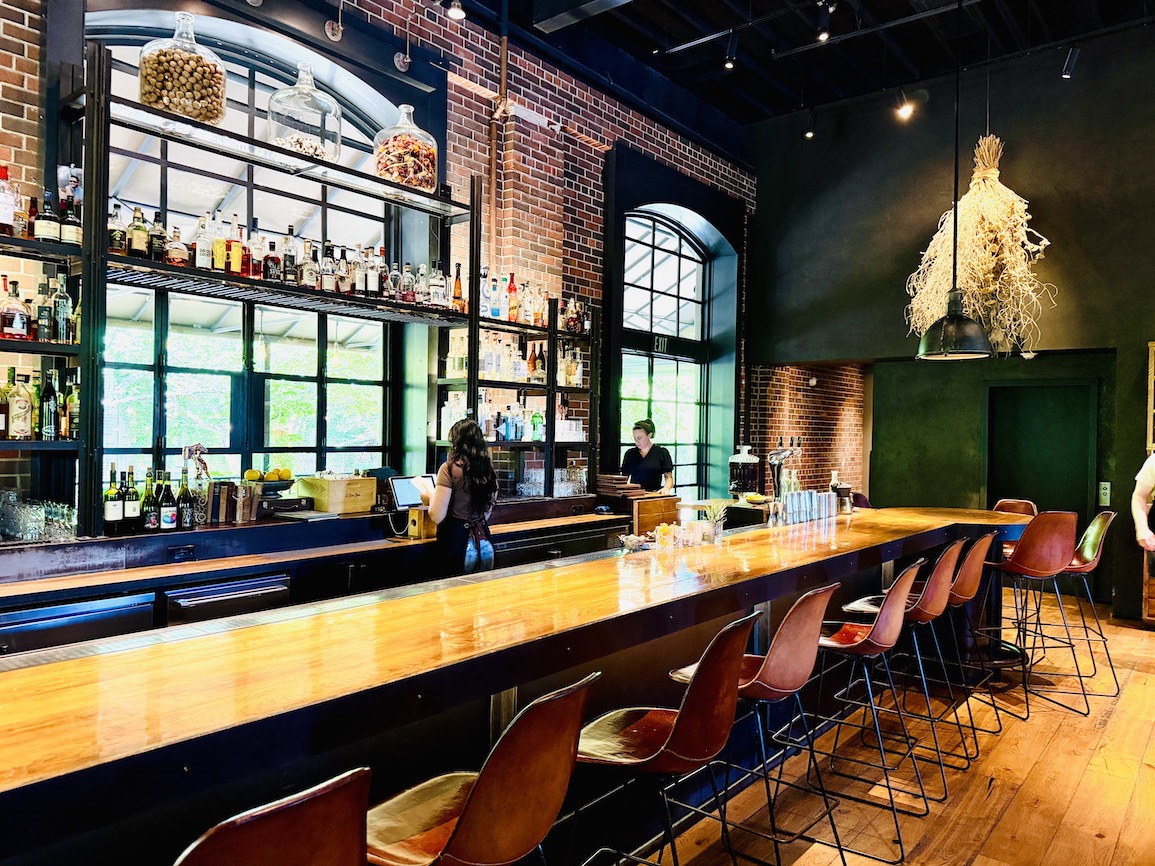 A sleek bar area at The Charter Oak, featuring a wide selection of spirits and a staff member preparing drinks.