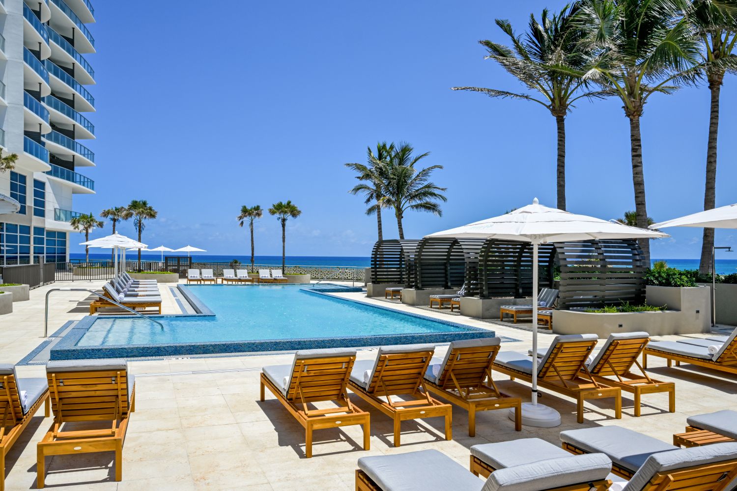 Sun loungers surround a tranquil pool with palm trees and ocean views at Amrit Ocean Resort on Florida’s Singer Island.